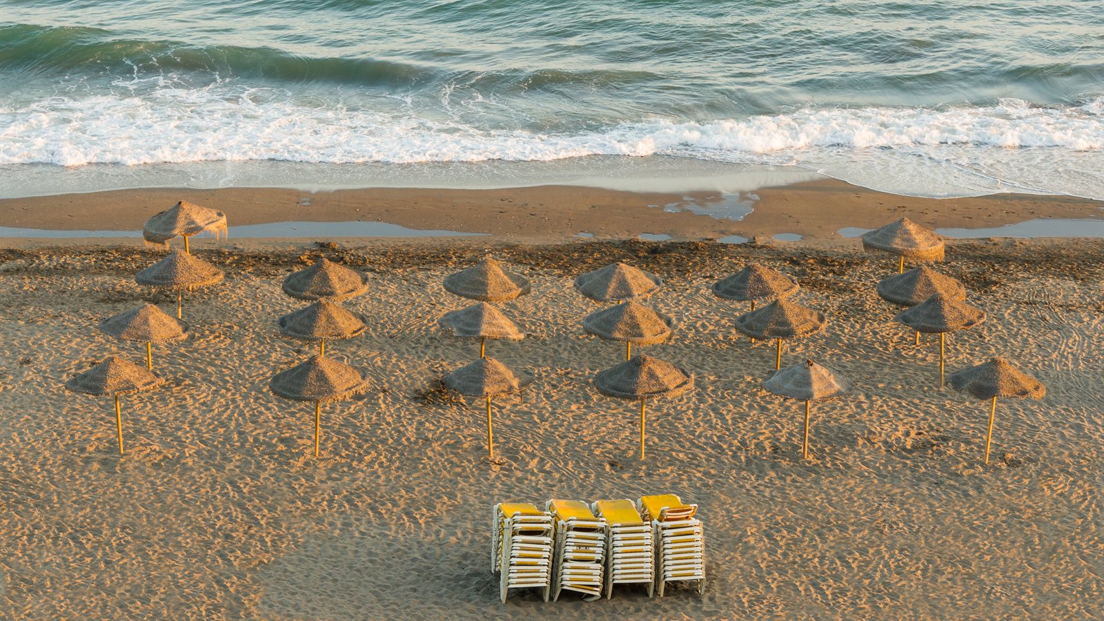Straw parasols and stacked loungers on a smooth evening beach